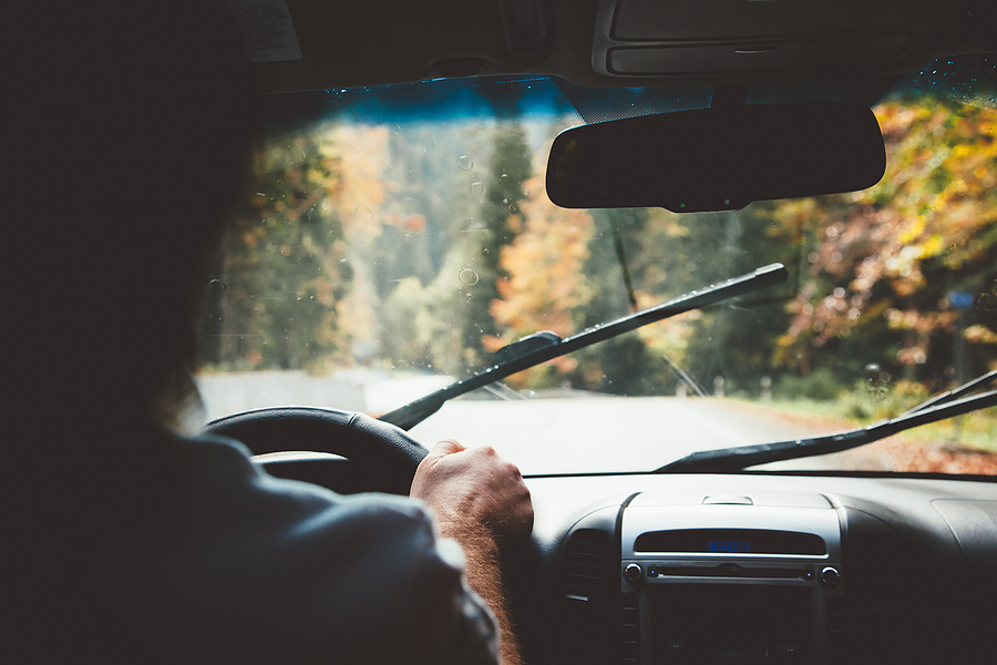 Man driving car in rain weather. Fall trip. Wipers cleaning windshield. Freedom travel concept. Autumn weekend.